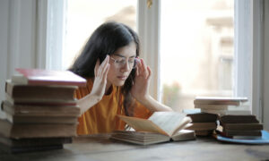 Woman reading a book at a desk with her hands on her temples